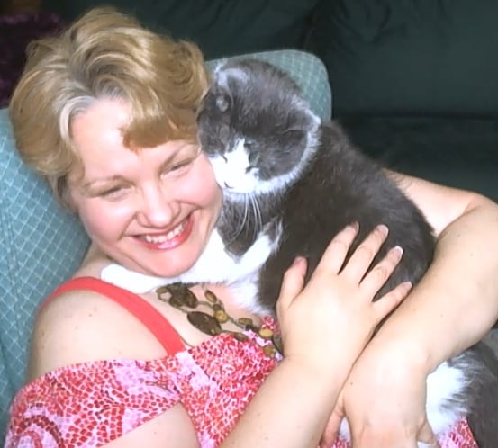 Andrea wearing a pink shirt sits holding her cat Owie near her face.