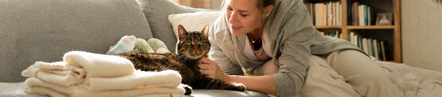 Woman sitting on a sofa, stroking and talking to a tabby cat lying beside her