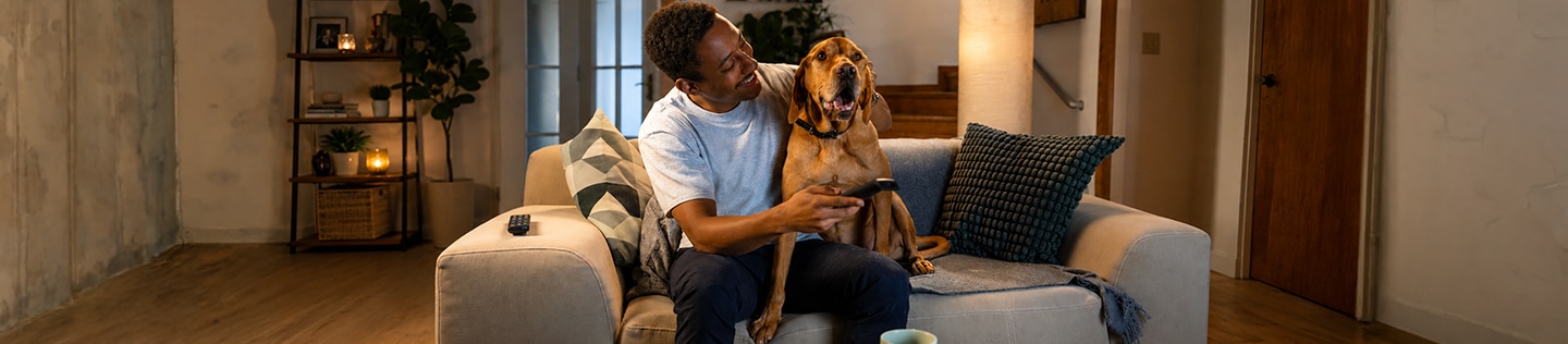 Large tan dog with floppy ears sitting across its owner’s lap on the sofa