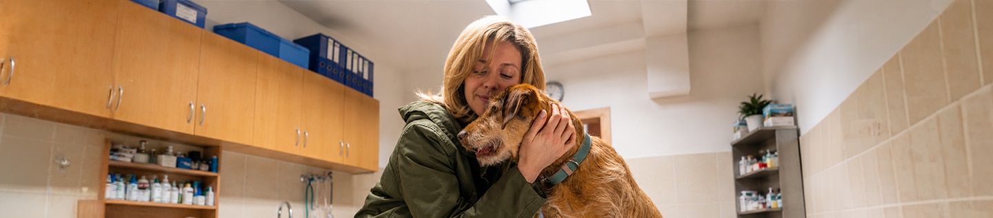 Woman smiling with her eyes closed as she cuddles a medium-sized, tan dog